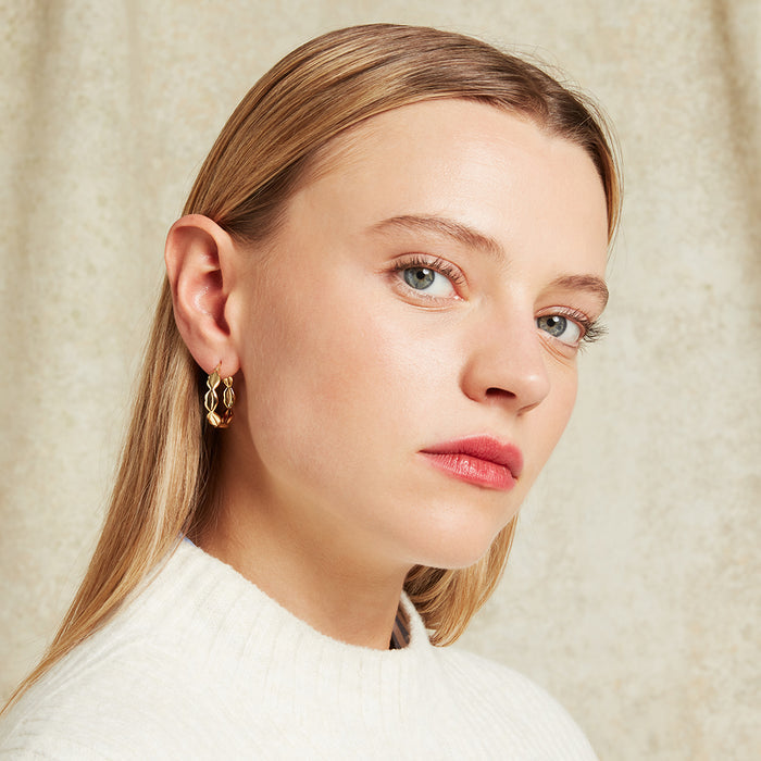 Close-up of a woman wearing gold hoop earrings against a beige background