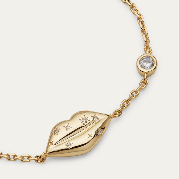 Gold bracelet with lip charm and inset crystals on a light gray background