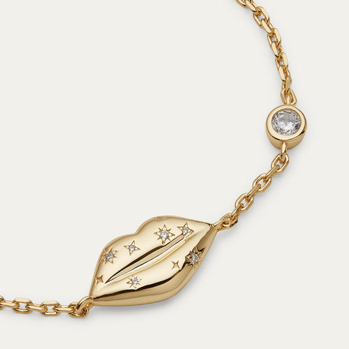 Gold bracelet with lip charm and inset crystals on a light gray background