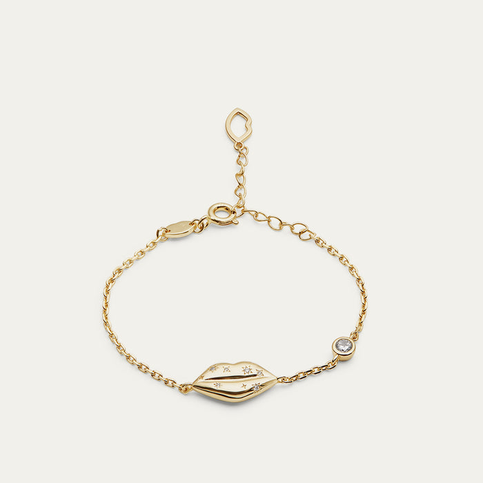 Gold bracelet with lip charm and inset crystals on a light gray background