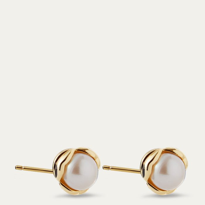 Pair of gold stud earrings with white pearls on a light beige background