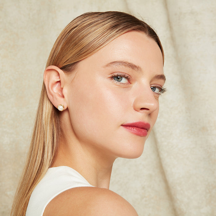 Close-up of a woman wearing gold and pearl stud earrings with a neutral background