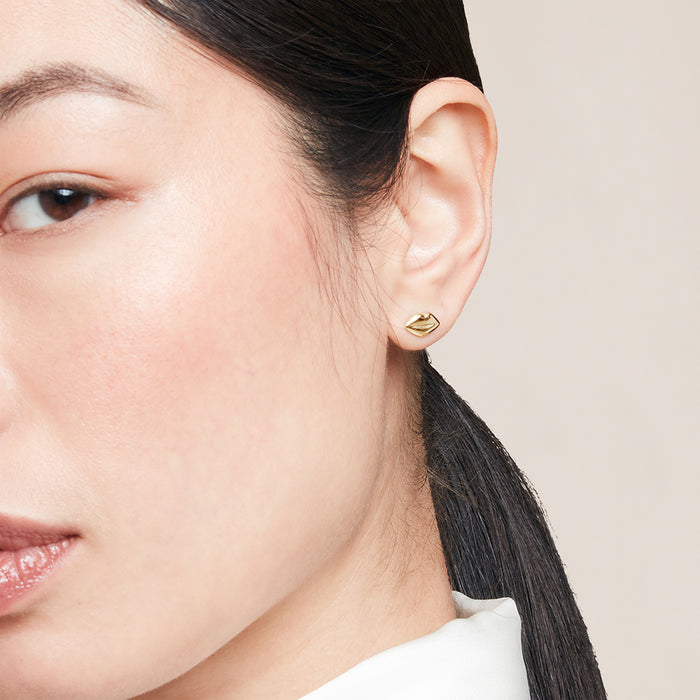 Close-up of a person wearing gold lip-shaped stud earring against a neutral background