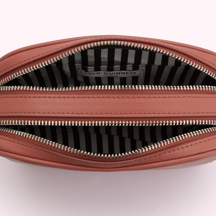Interior of a dusty rose Lulu Guinness crossbody bag with black and white striped lining.