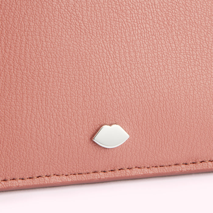 Close-up of a dusty rose-coloured leather wallet with a silver lip-shaped emblem.