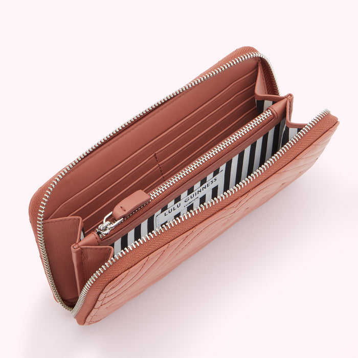 Dusty rose quilted zip-around wallet by Lulu Guinness, open to show interior with black and white striped lining.