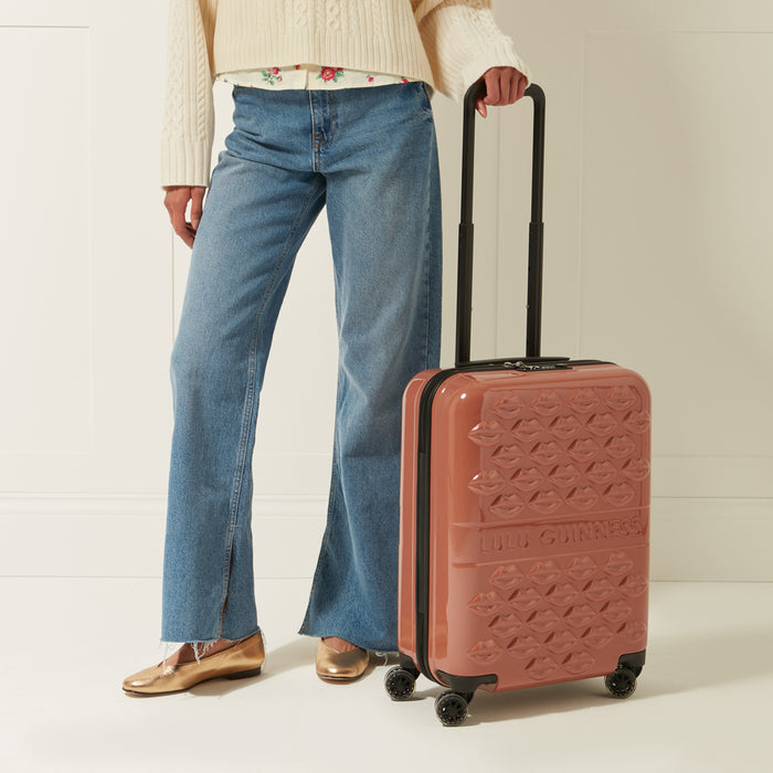 Woman in jeans holding a dusty rose Lulu Guinness lips-printed carry-on suitcase.