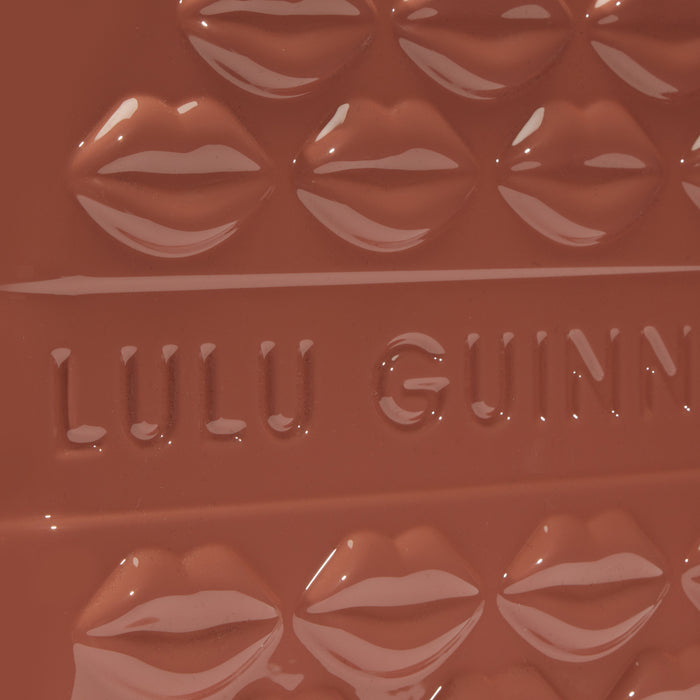 Close-up of a mauve-toned Lulu Guinness makeup product with embossed lips and logo.