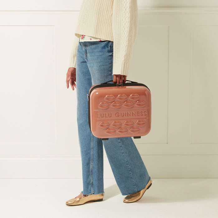 Person carrying a pink Lulu Guinness makeup case with lips design against a white background.