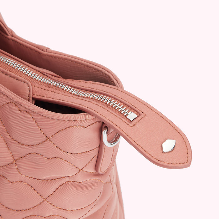 Close-up of a dusty rose quilted handbag's zipper and pull tab, showcasing the bag's texture and detailing.