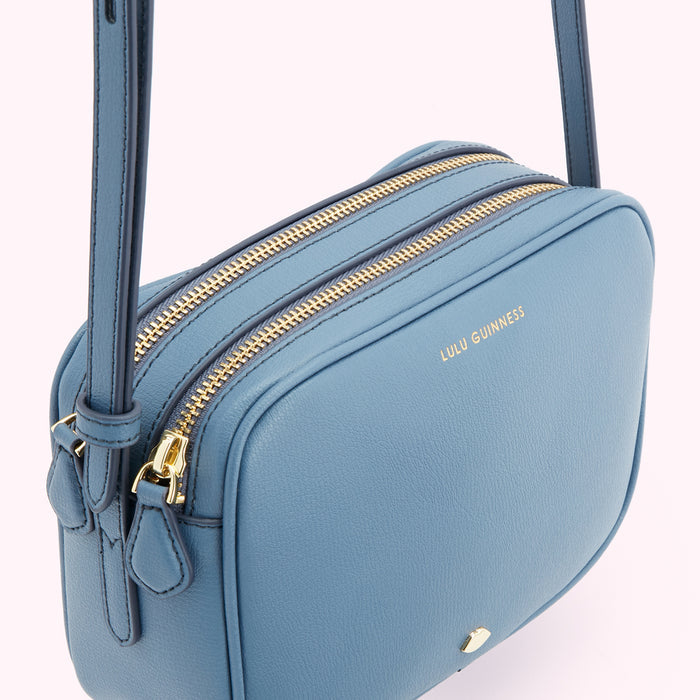 A powder blue Lulu Guinness crossbody bag with two gold zippers.