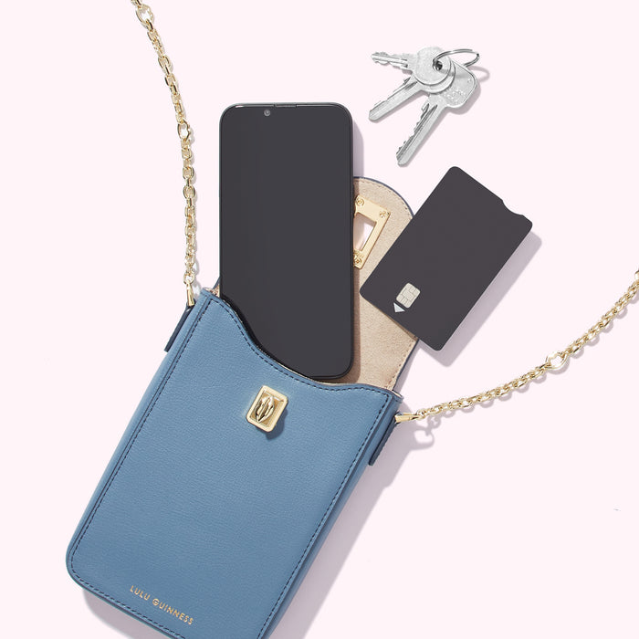 A powder blue Lulu Guinness crossbody phone bag with a gold chain strap, containing a smartphone, keys, and a card.