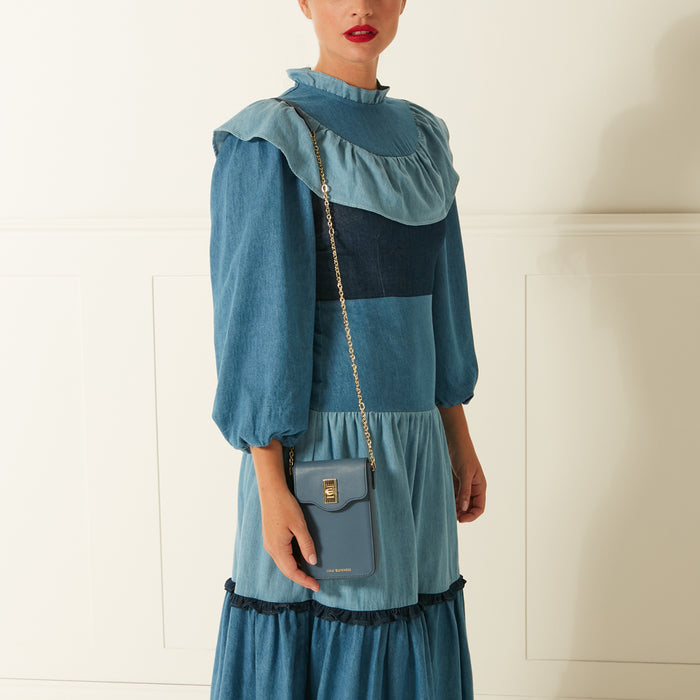 Woman in a blue denim dress holding a small blue crossbody bag.