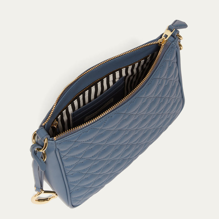 Blue quilted handbag with gold zipper open to reveal a striped lining on a white background