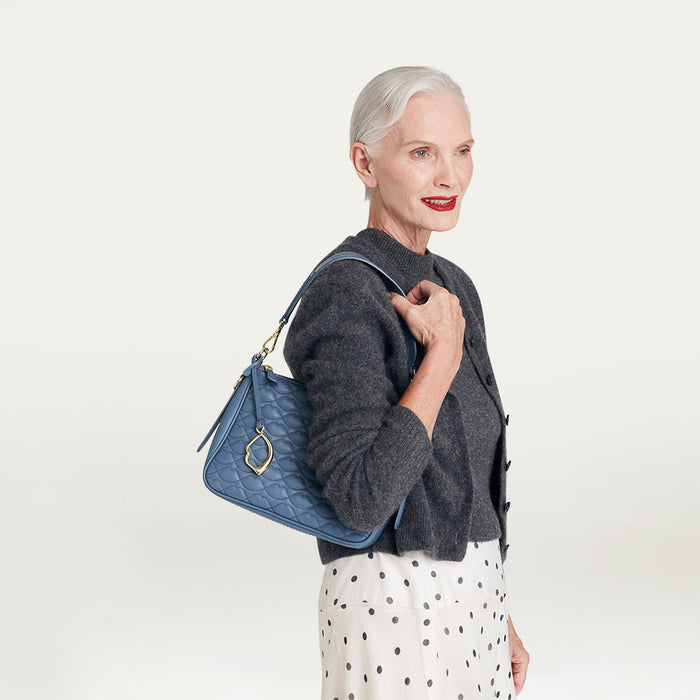 Woman holding a blue quilted shoulder handbag against a light gray background