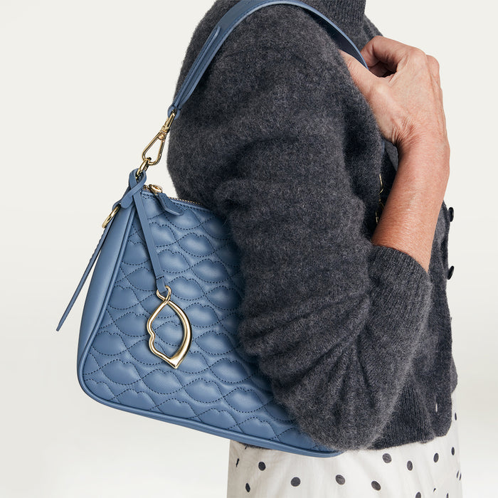Person holding a blue quilted handbag with a gold clasp against a neutral background