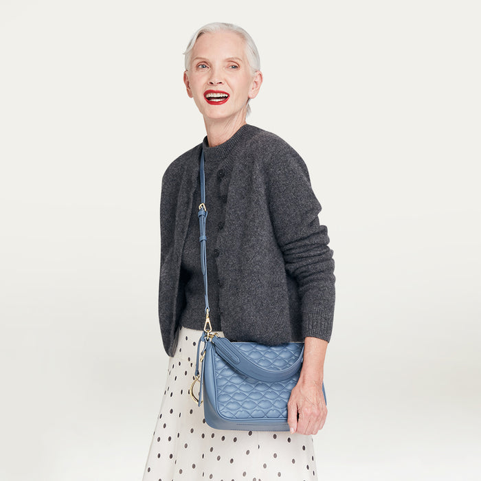 Woman holding a blue quilted crossbody handbag against a light gray background