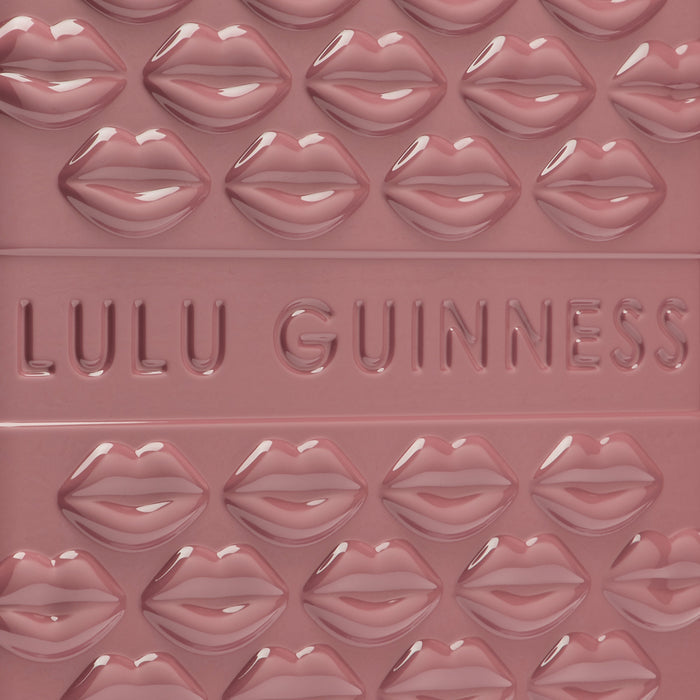 Close-up of a dusky rose Lulu Guinness product featuring a repeating pattern of embossed lips and the brand name in a recessed design.