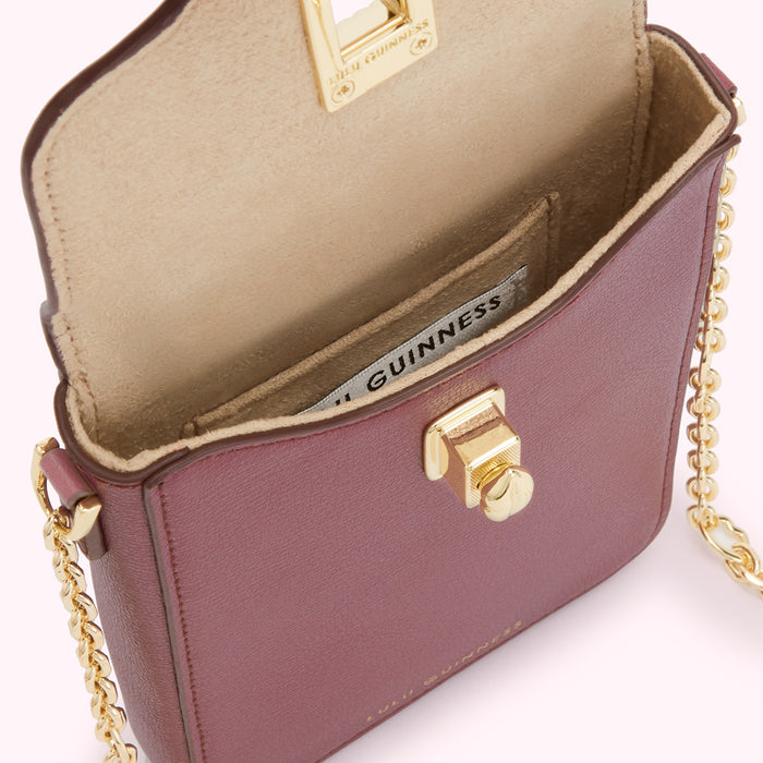 Close-up view of a burgundy Lulu Guinness handbag with a gold clasp and chain strap, the interior is beige with the brand name visible.