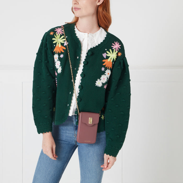 A woman in a green floral cardigan is modelling a mauve crossbody phone bag.
