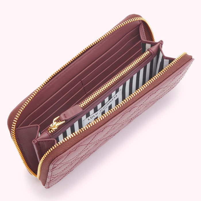 Open burgundy quilted zip-around wallet by Lulu Guinness, featuring a black and white striped interior.