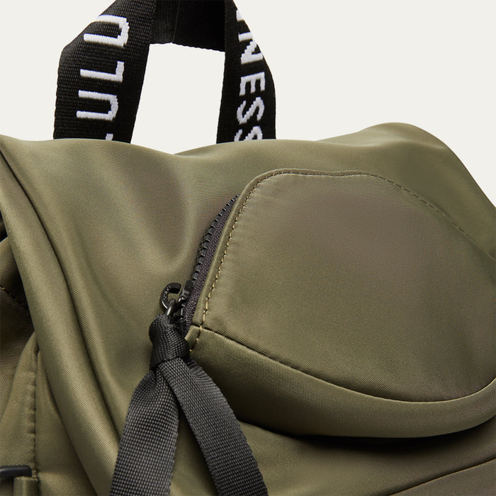 Close-up of a green backpack with a black strap on a light grey background