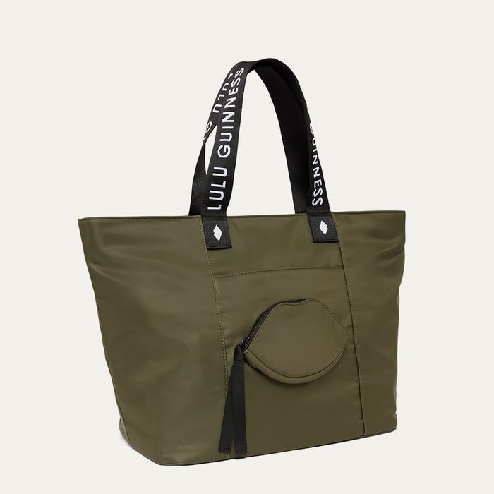 Green tote bag with black handles and a lip-shaped pocket on the front on a white background