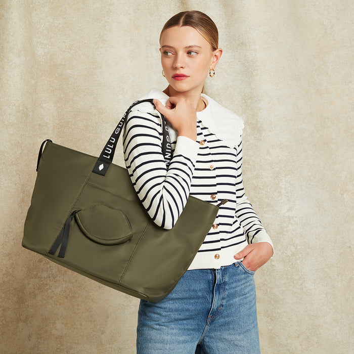 Woman holding a green tote bag on her shoulder against a beige background