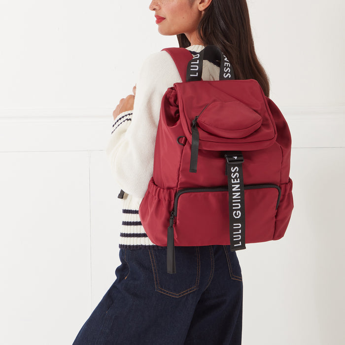 Woman wearing a maroon Lulu Guinness backpack against a white background.