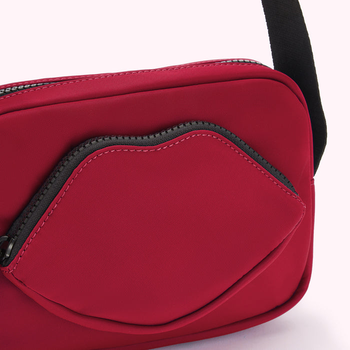 Close-up of a crimson red crossbody bag with a lip-shaped zipper pocket.