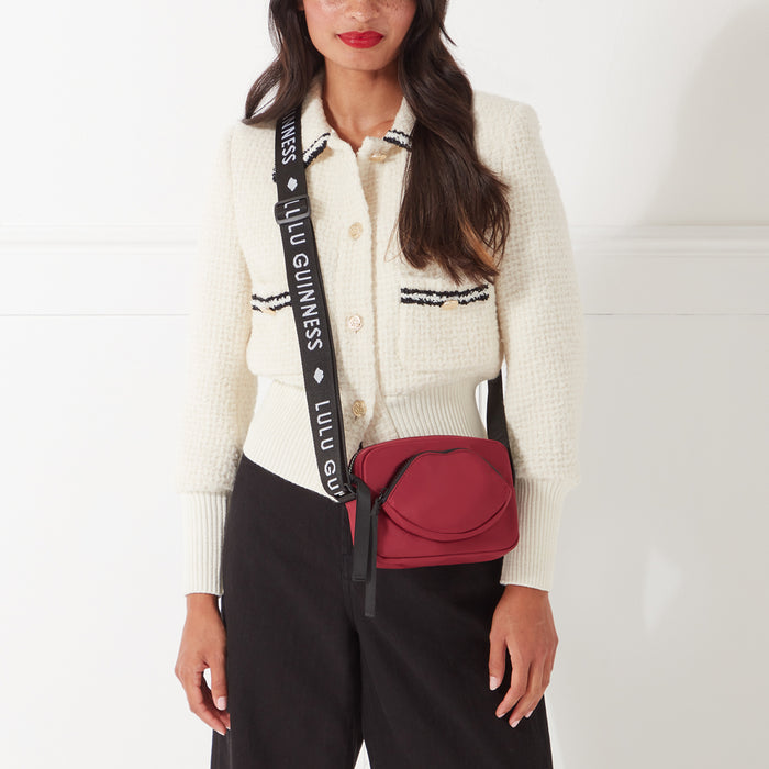 Woman wearing a cream cardigan and black pants, modelling a maroon Lulu Guinness lip-shaped crossbody bag with a black strap.