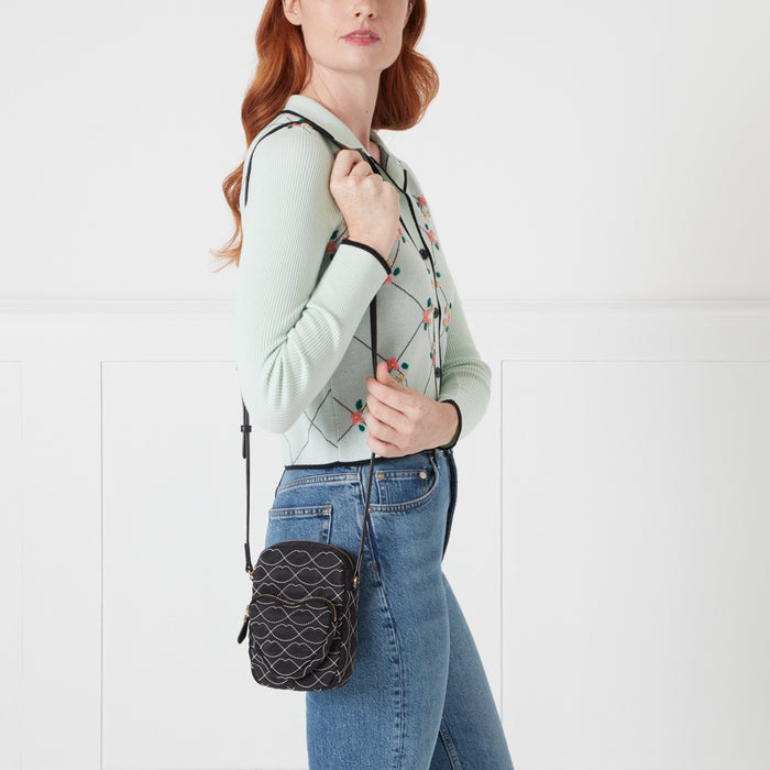 Woman in mint green cardigan holding black quilted crossbody bag against white background.