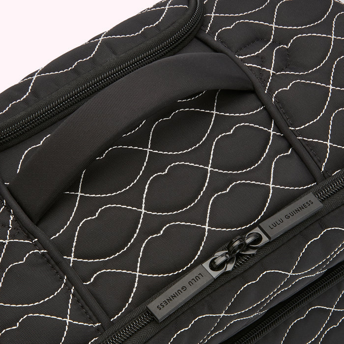 Close-up of a black Lulu Guinness quilted travel bag with a white lip print pattern, showing the top handle and zipper.