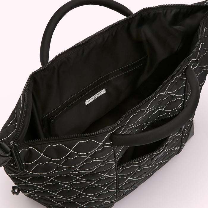 Black quilted Lulu Guinness travel bag with white stitching, shown open to reveal the interior and a small zipped pocket.