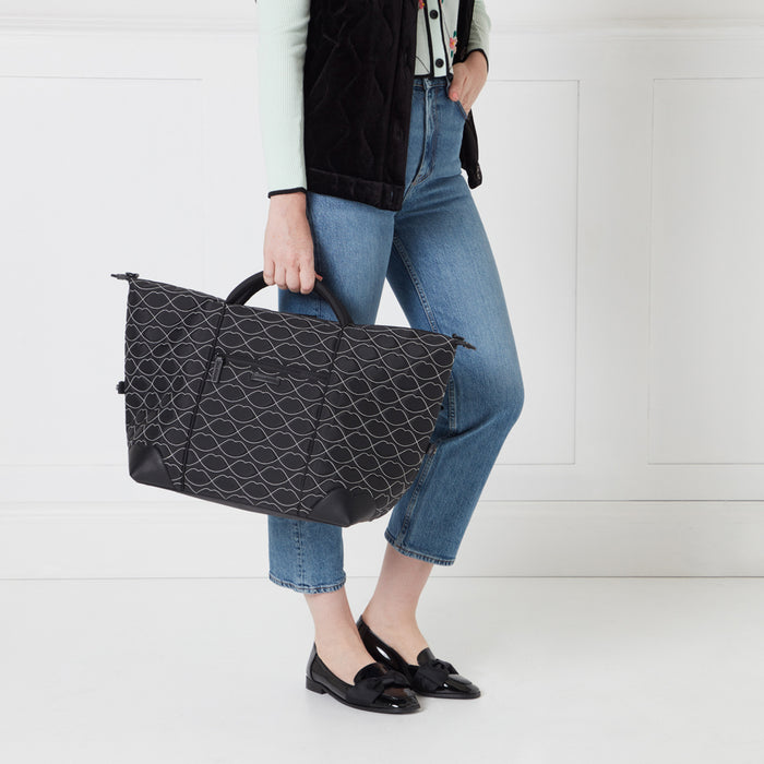 Woman holding a black and white patterned bag in front of a white wall.