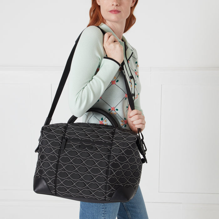 A woman holds a black quilted bag with a lip print pattern against a white background.