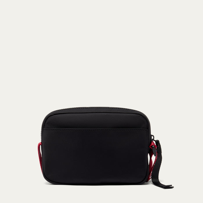 Black crossbody bag with red accents on a light grey background