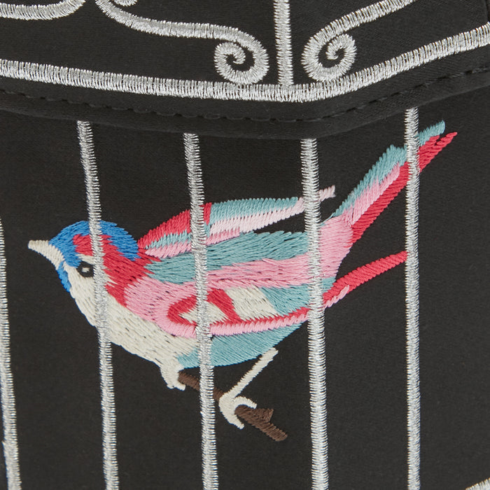 Close-up of embroidered bird in cage on black fabric with silver accents.