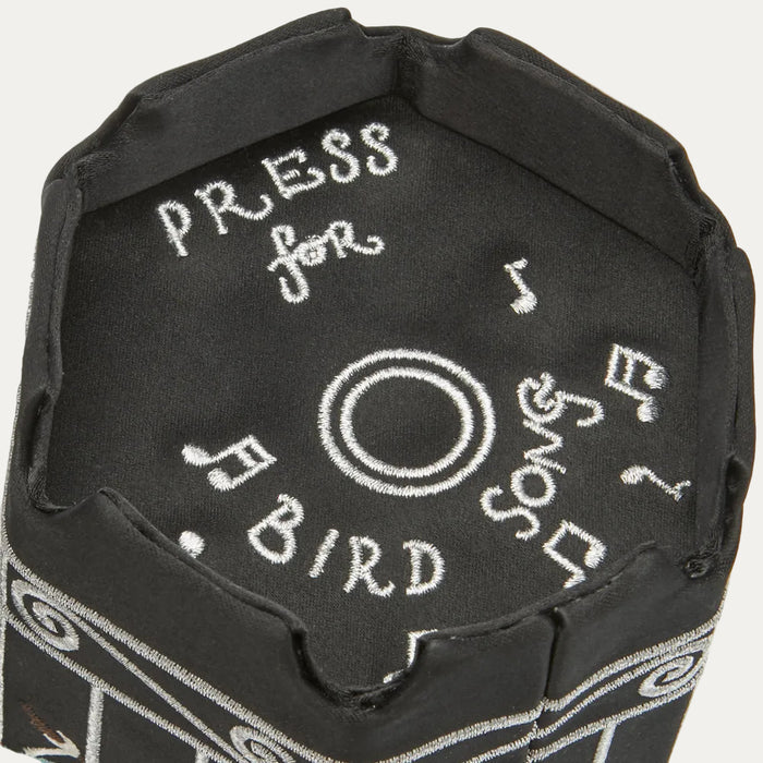 Close-up of a black fabric item with embroidered text "PRESS for BIRD Song" and musical notes.