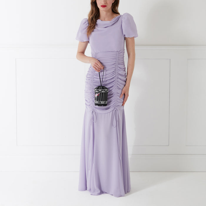 Woman in lavender dress holding a black birdcage-shaped purse against a white background.
