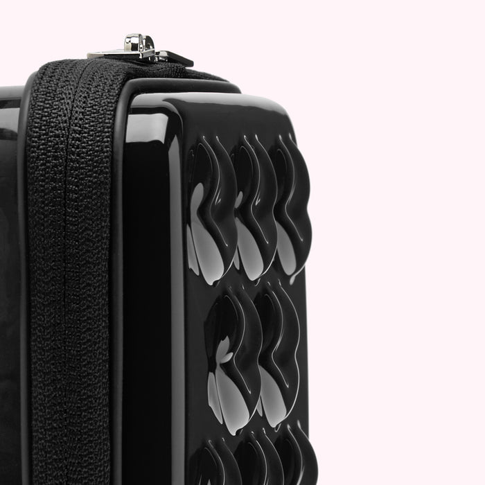 Close-up of a black, glossy rectangular bag with a textured surface and zipper.