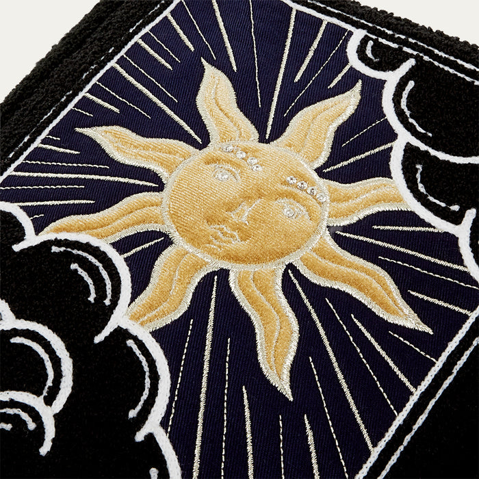 Close-up of a tote bag with a embroidered sun design on a dark background with decorative elements.