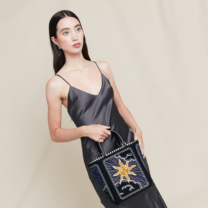 Woman holding a black handbag with a sun and moon design on a beige background