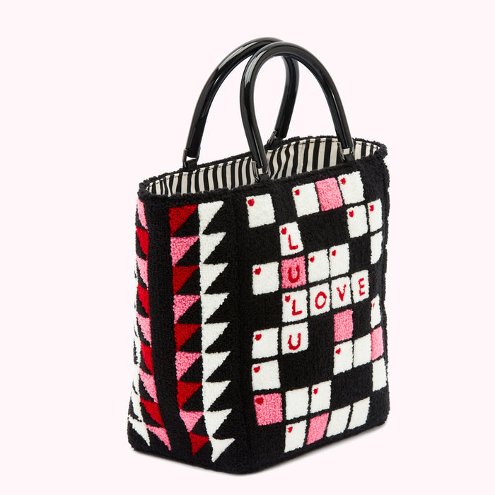 Black and white crossword puzzle tote bag with pink and red accents on a white background. The bag has black handles and says "LOVE LULU" in the crossword puzzle.