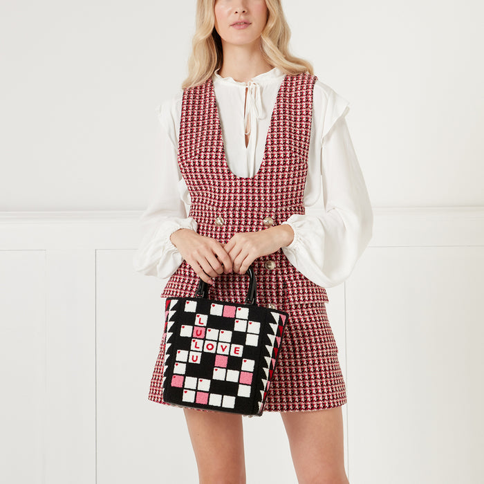 Woman in red and white checkered dress holding a black and white crossword-style handbag that says "LOVE LULU" on a white background.