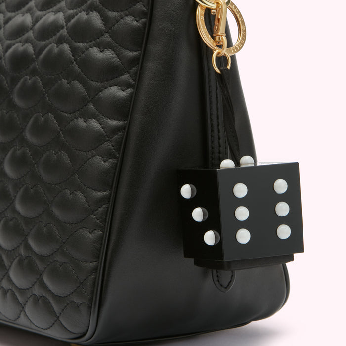 Close-up of a black quilted leather handbag with a black die-shaped charm featuring white dots.
