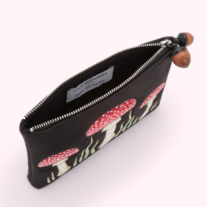 Black silk pouch embroidered with red and white mushrooms and green grass, accented with acorn zipper pulls. The inside shows a Lulu Guinness x Bell Hutley label.