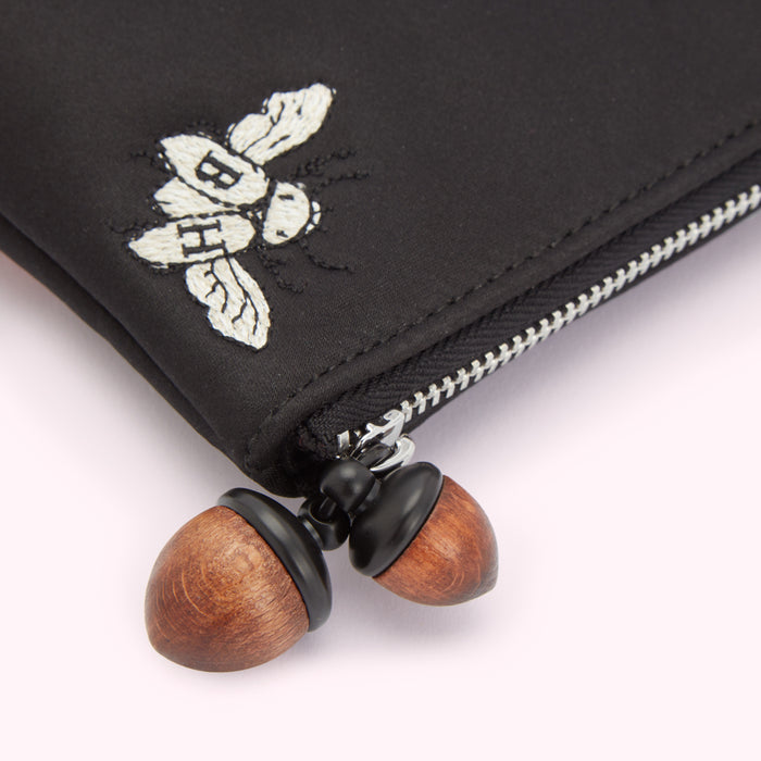 Close-up of a black pouch with an embroidered bee and wooden acorn zipper pulls.