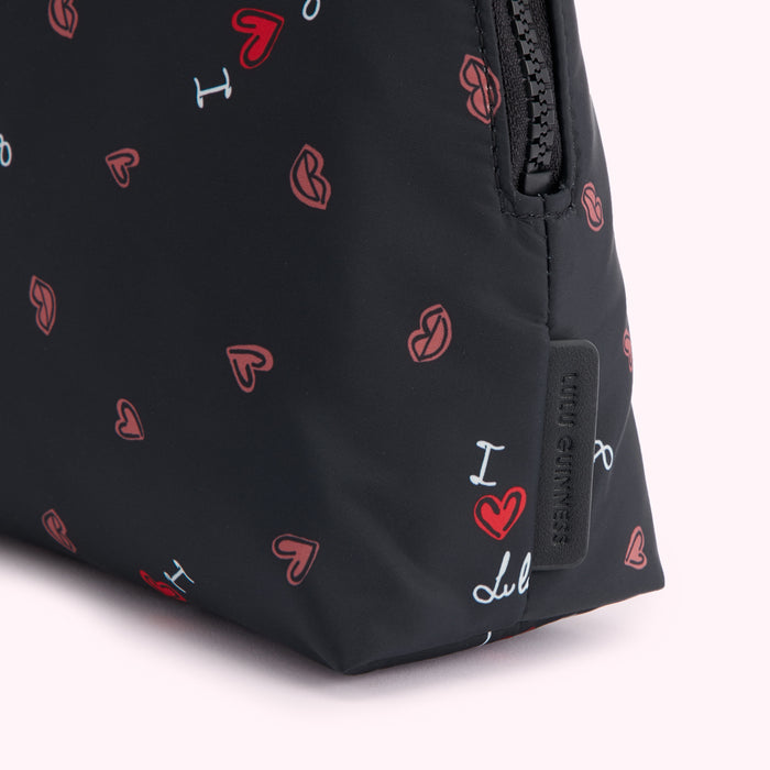 Close-up of a black Lulu Guinness cosmetic bag with a zipper closure and a repeating pattern of hearts and lips.
