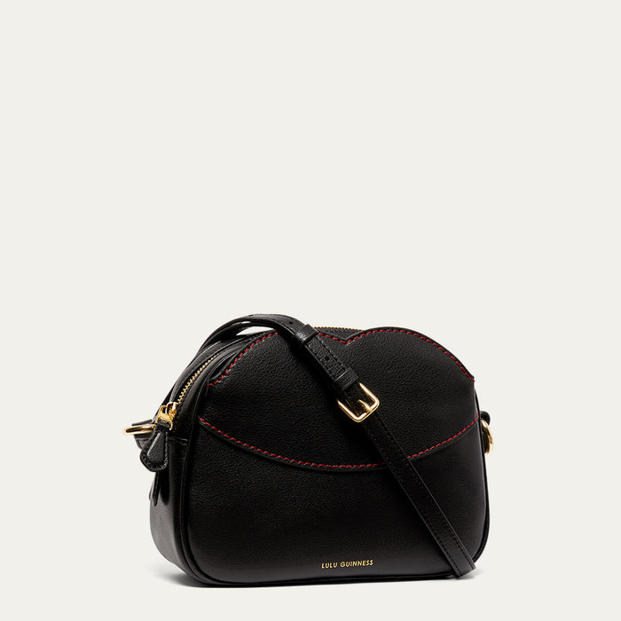 Black leather crossbody handbag with red stitching and gold accents on a light grey background